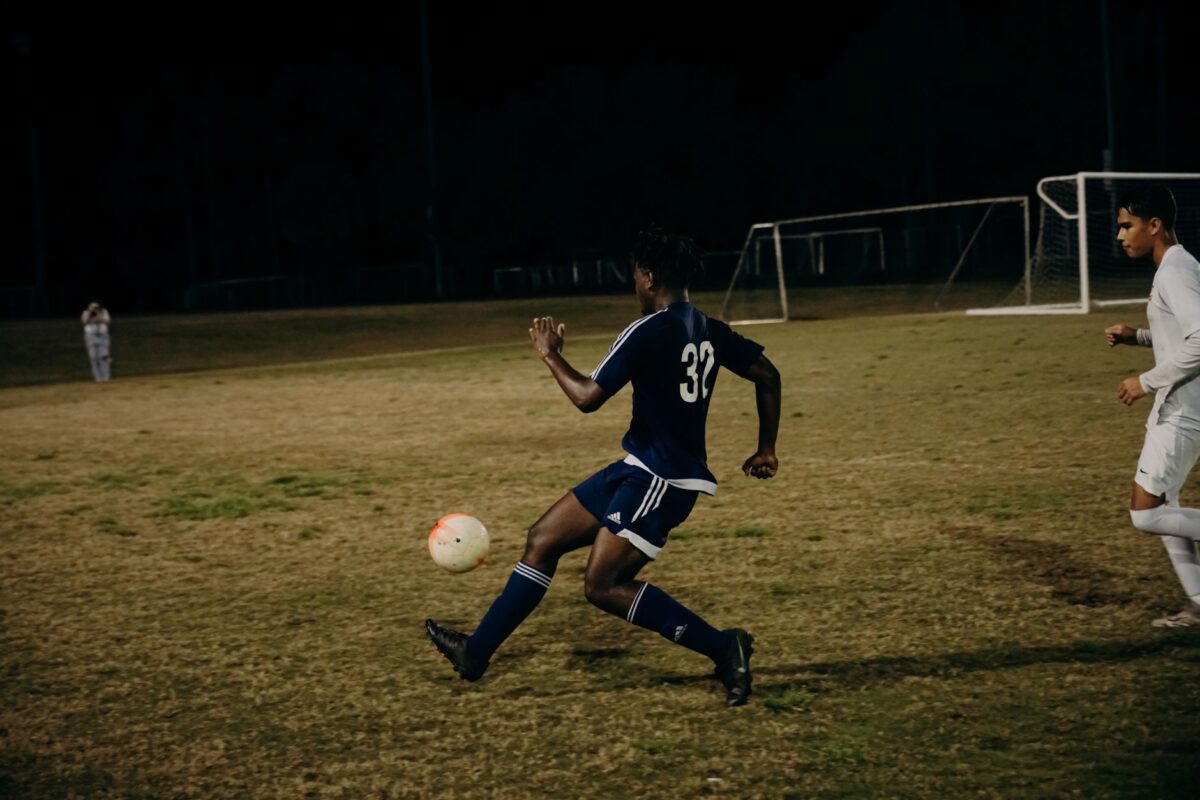 Two players compete fiercely during a nighttime football match on a grass field.