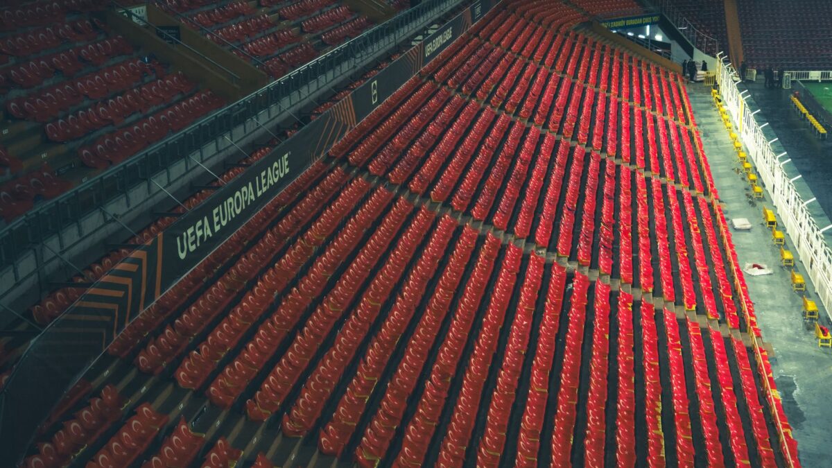 Rows of empty red seats in a UEFA Europa League stadium, captured from above. (photo Pexels)