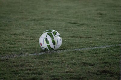 A soccer ball resting on a grass field, captured during nightfall with visible dew.